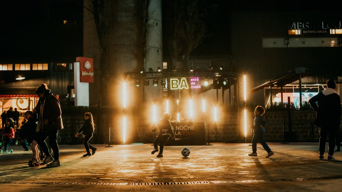 Children enjoying a night soccer game at an outdoor urban event with festive lighting.